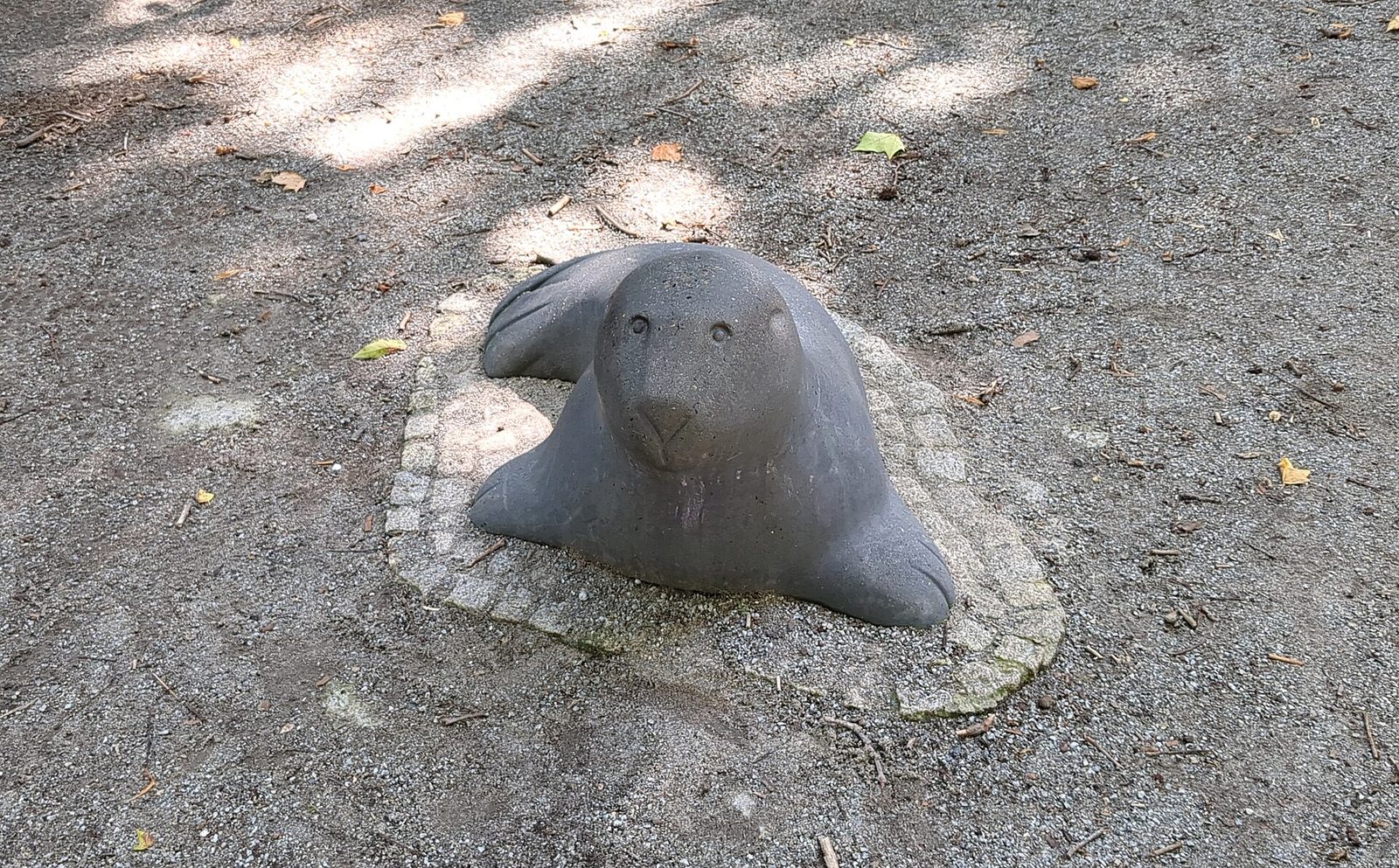 Betongskulptur formet som en sel på en lekeplass i Berlin, plassert på grusunderlag i lett skygge