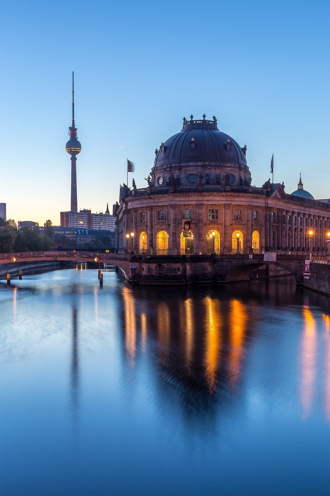 Bode-Museum opplyst i blatimen med Fernsehturm og en manesigd bak