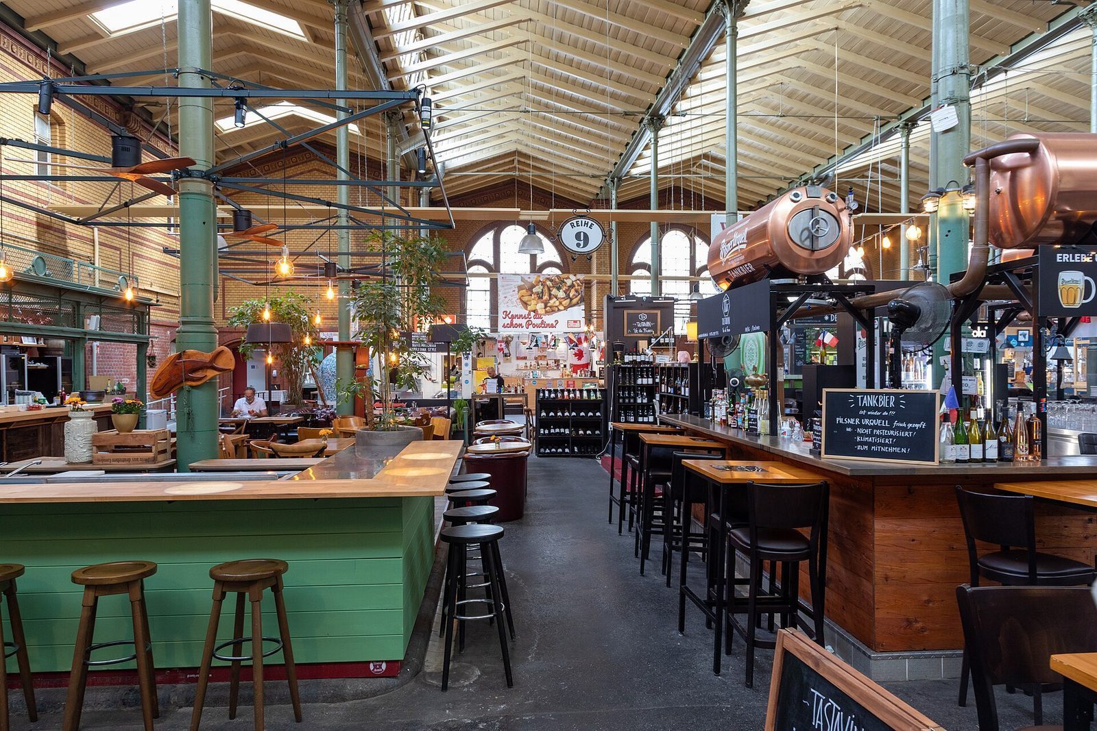 Innsiden av Arminius-Markthalle med gronne stopejernssoyler, takstoler i tre og barkranker
