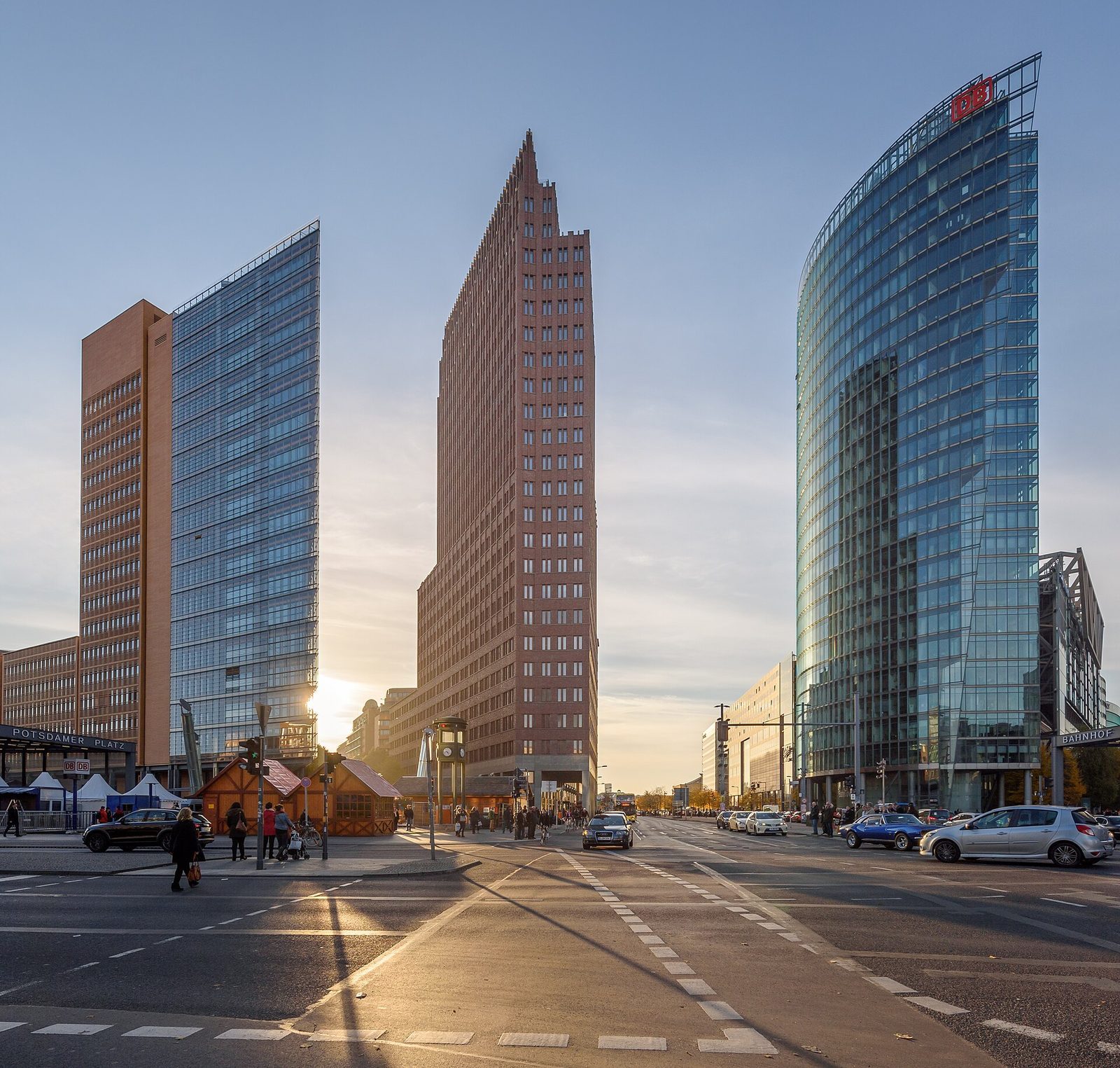 Kollhoff-tarnet og Bahntower pa Potsdamer Platz i motlys, med markedsboder ved stasjonen