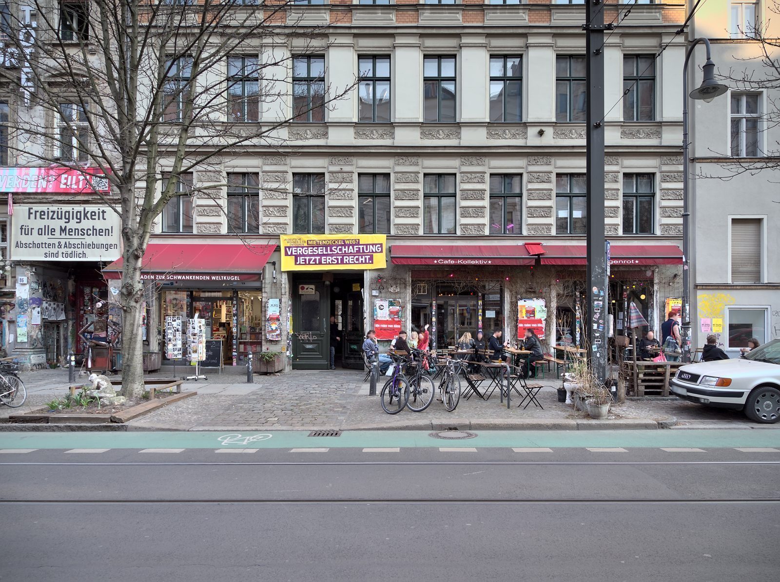 Kafeer og smabutikker i gateplanet pa Kastanienallee, med sykkelfelt og trikkeskinner foran