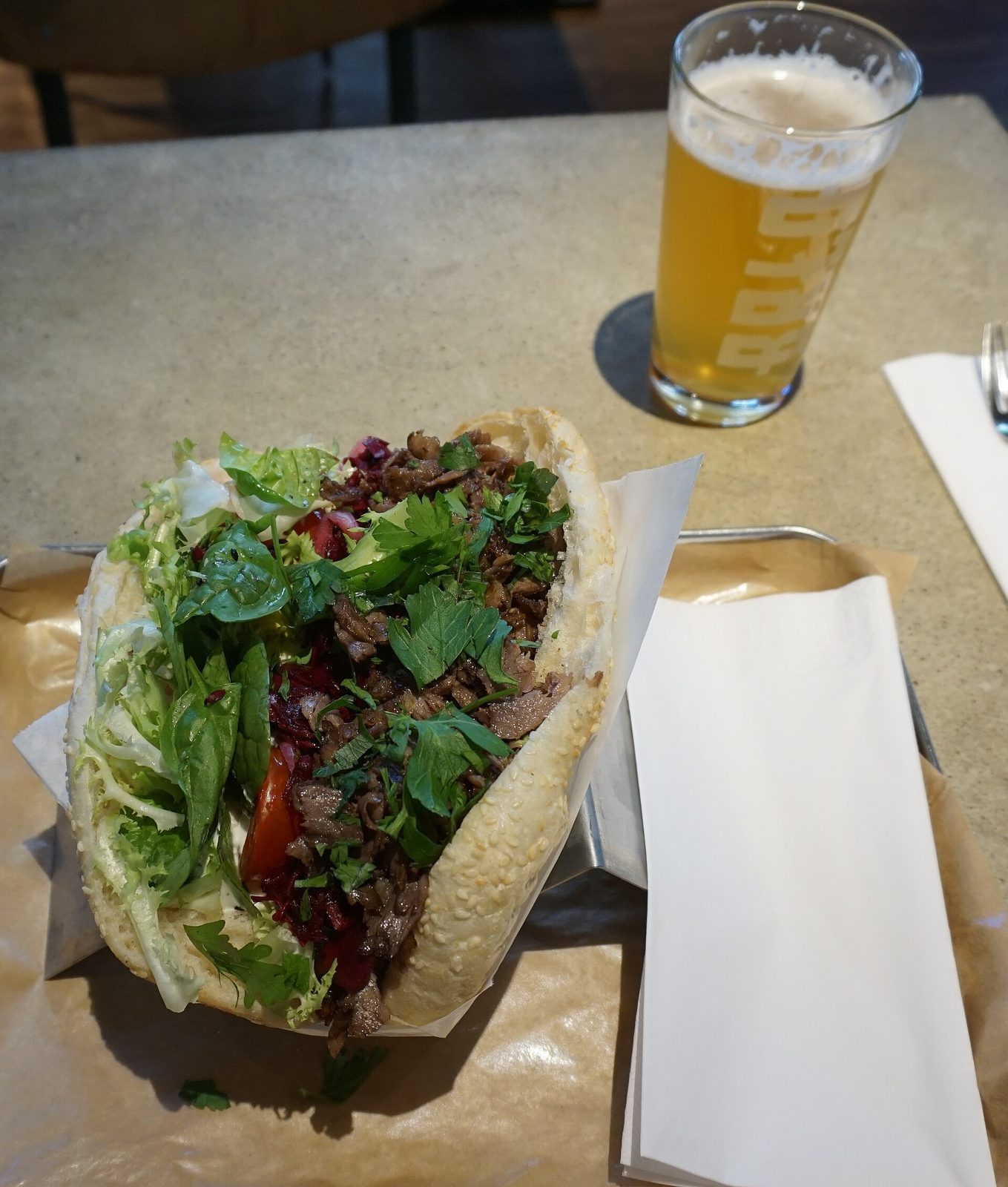 Döner i brød med salat og saus, servert med et glass øl ved siden av