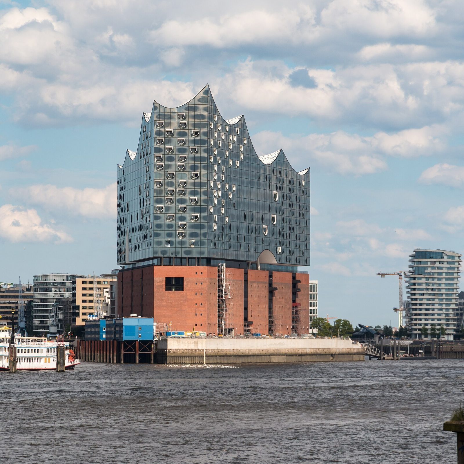 Elbphilharmonie i Hamburg sett fra vannet, med den bølgende glassfasaden på det gamle teglpakkhuset og en hjuldamper i havna