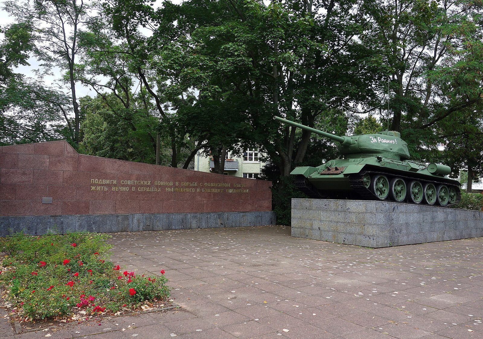 Sovjetisk T-34-stridsvogn pa sokkel ved en minnevegg med russisk innskrift i museumshagen i Karlshorst