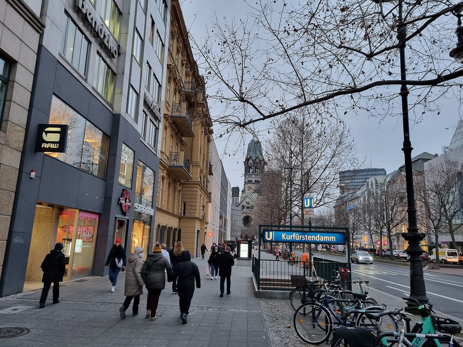 Kurfürstendamm på vinteren med U-baneskilt og Gedächtniskirche bakerst i gata