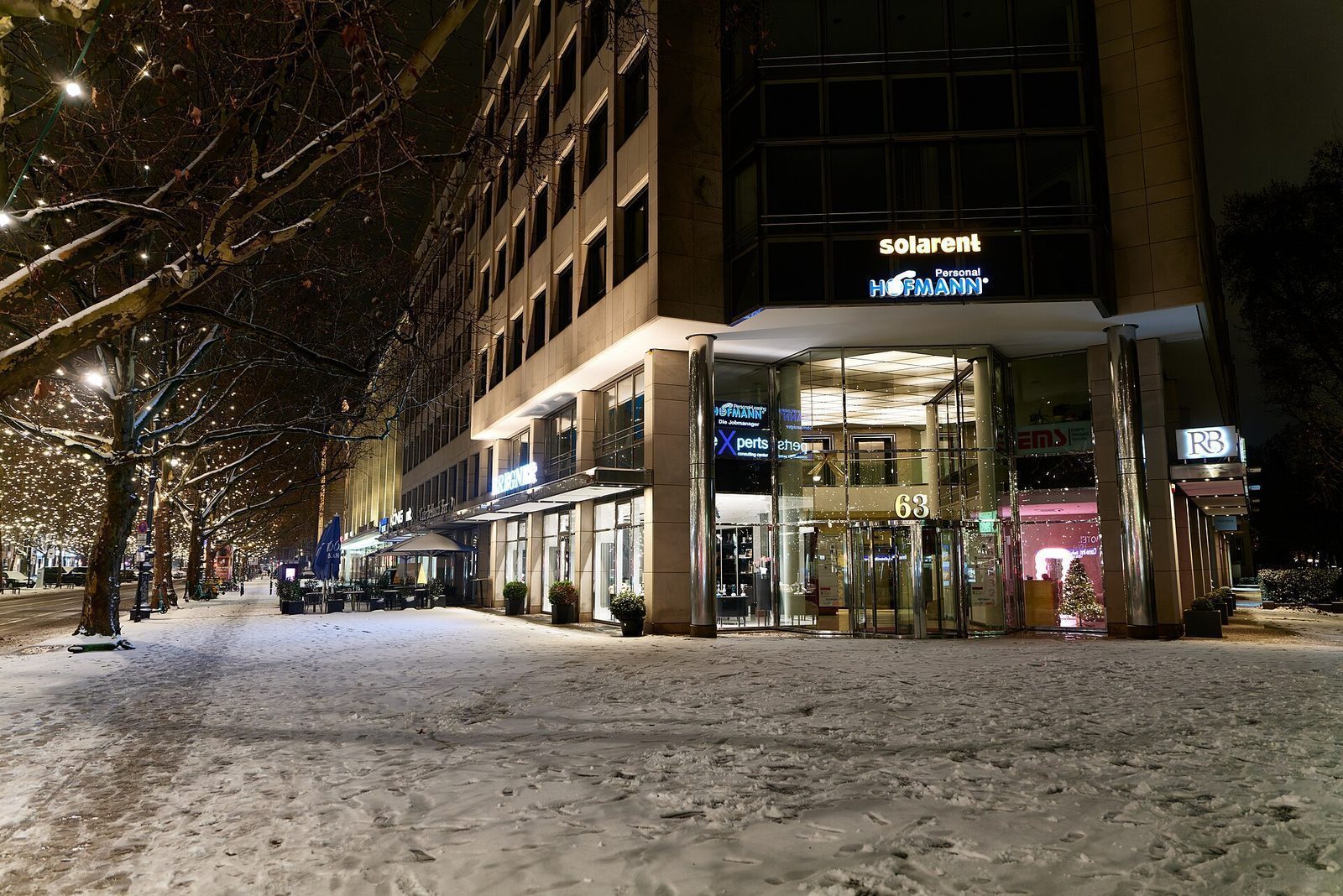 Snødekt fortau langs Kurfürstendamm en vinterkveld, med lysende butikkvinduer