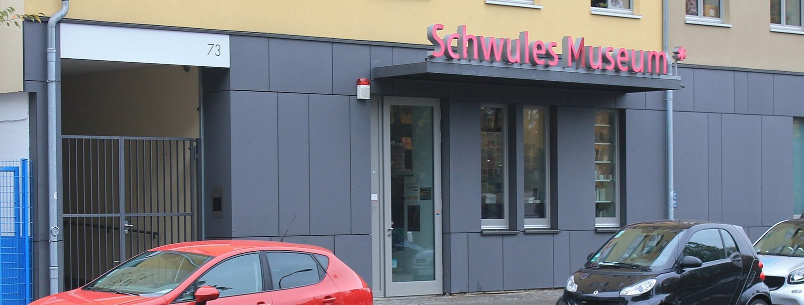 Gateinngangen til Schwules Museum i nummer 73, med det rosa navnetrekket over den grå fasaden og et utstillingsvindu med bøker