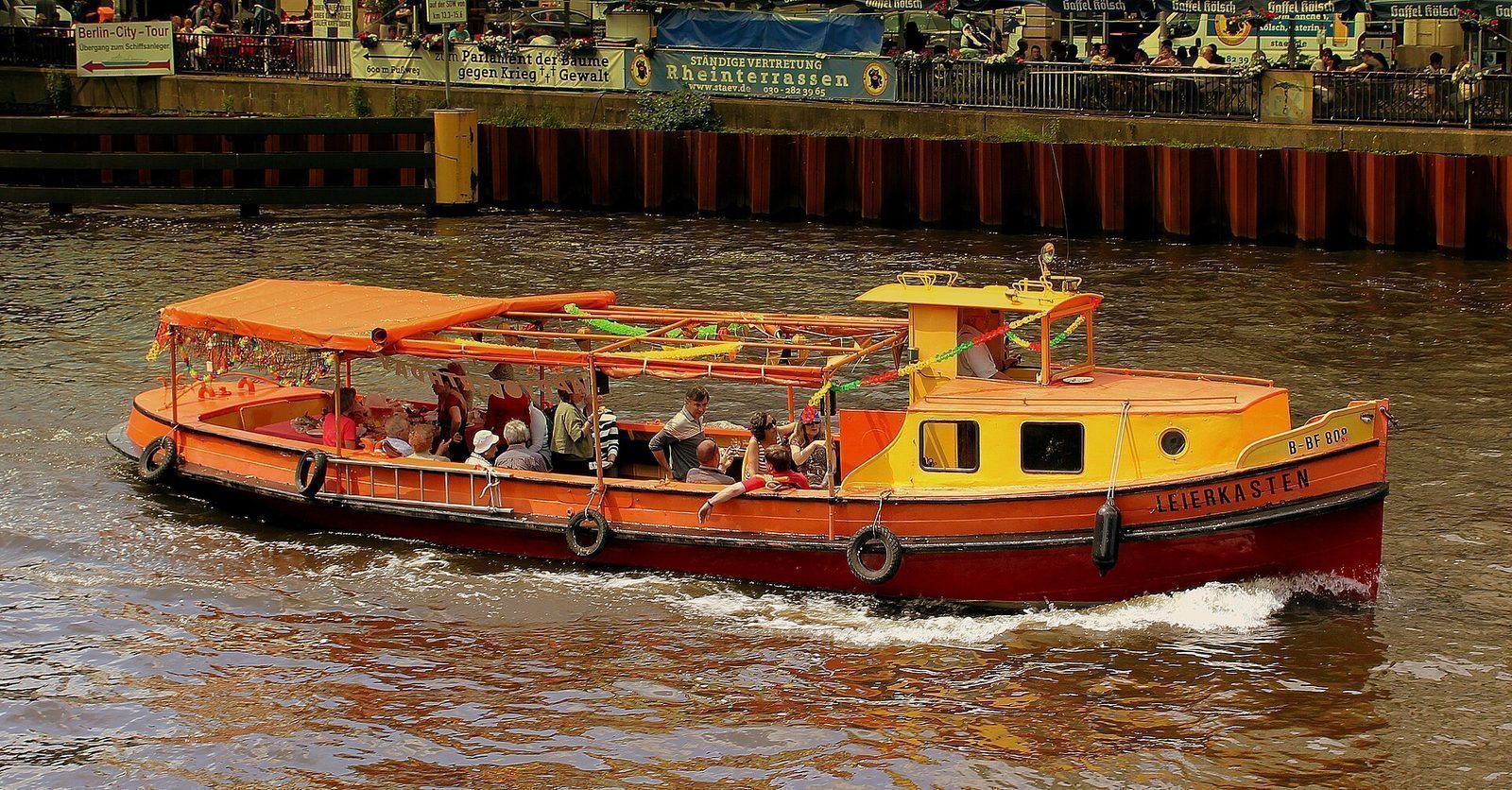 Utfluktsbåt med passasjerer på soldekket på vei nedover Spree