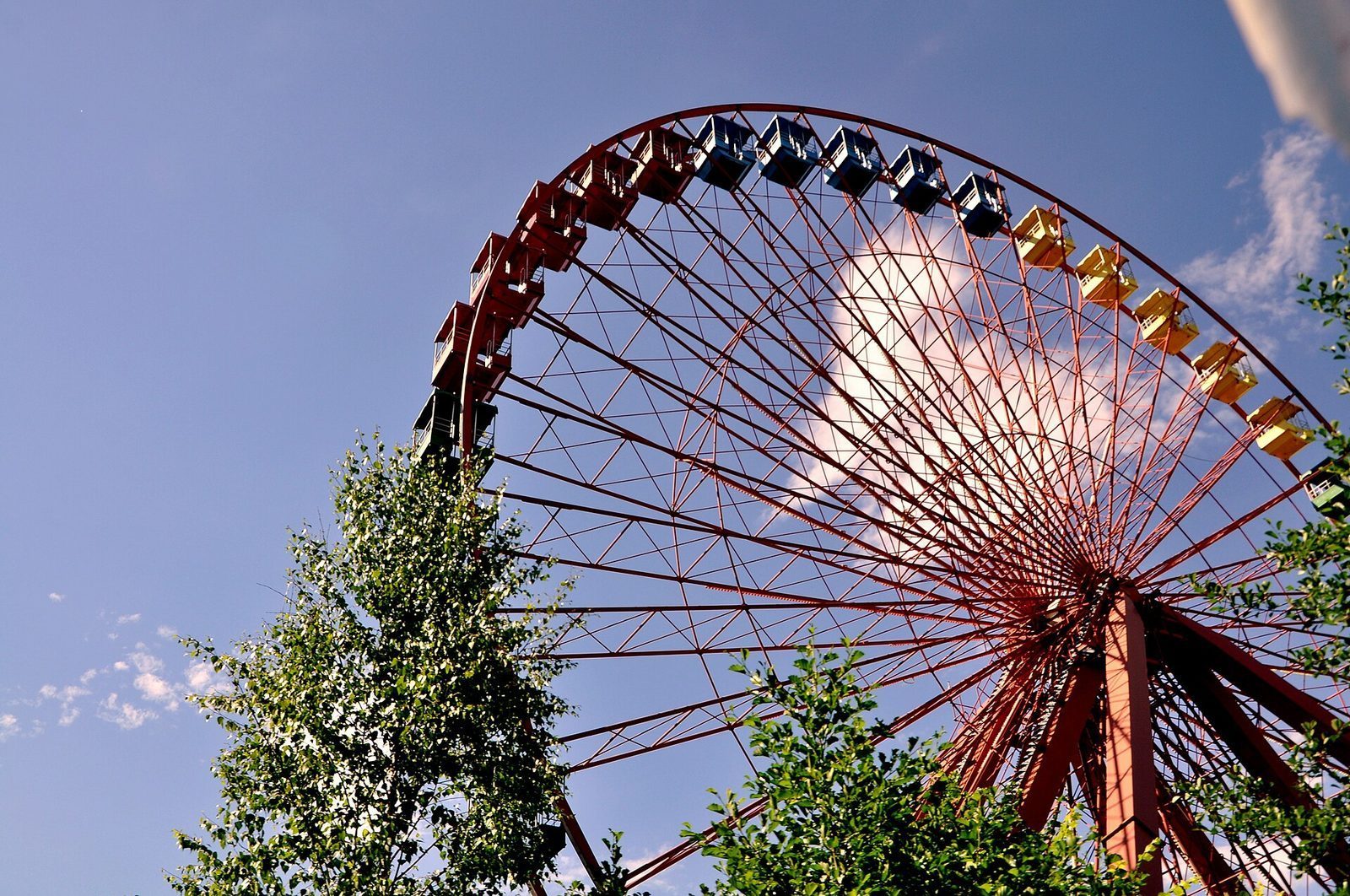 Det rustne pariserhjulet i Spreepark sett nedenfra en sommerdag, den røde stålkonstruksjonen mot blå himmel over grønne trær