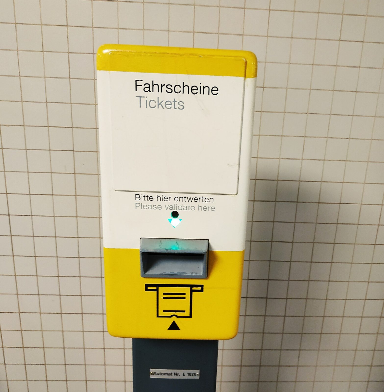 Gul billettvalidator med teksten Bitte hier entwerten og Please validate here over innstikket