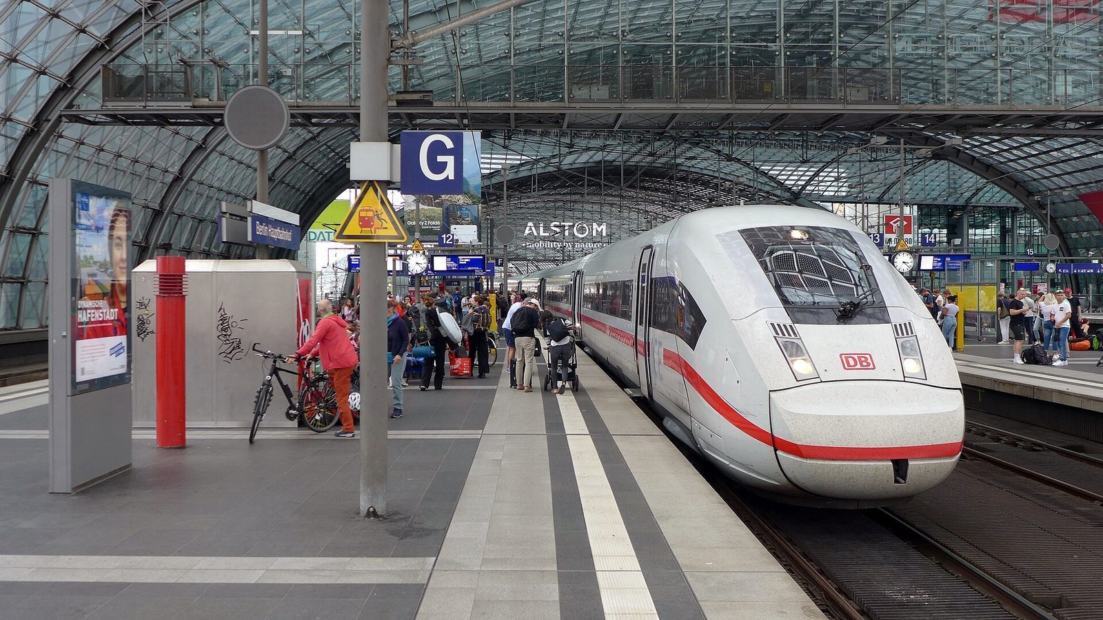 Hvitt ICE-tog med rod stripe ved perrongen i Berlin Hauptbahnhof, under buet glasstak