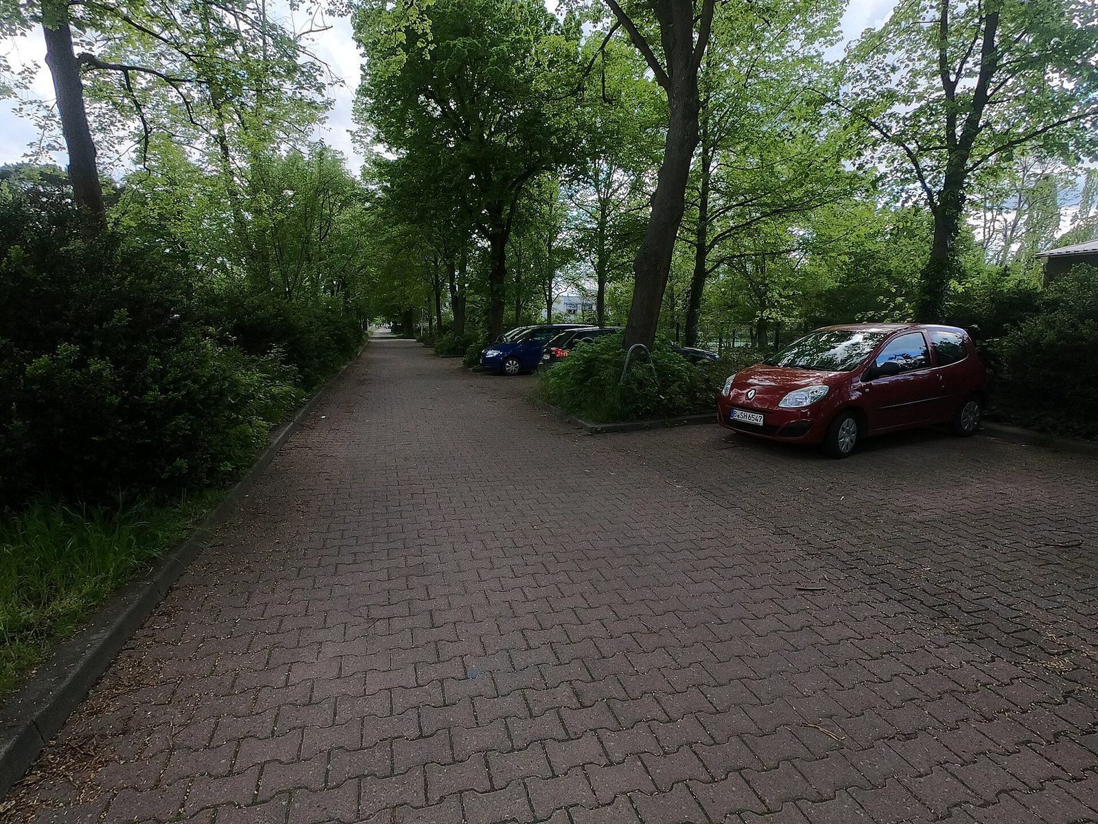 Rolig parkeringsomrade med brostein og parkerte biler under traer i utkanten av Berlin