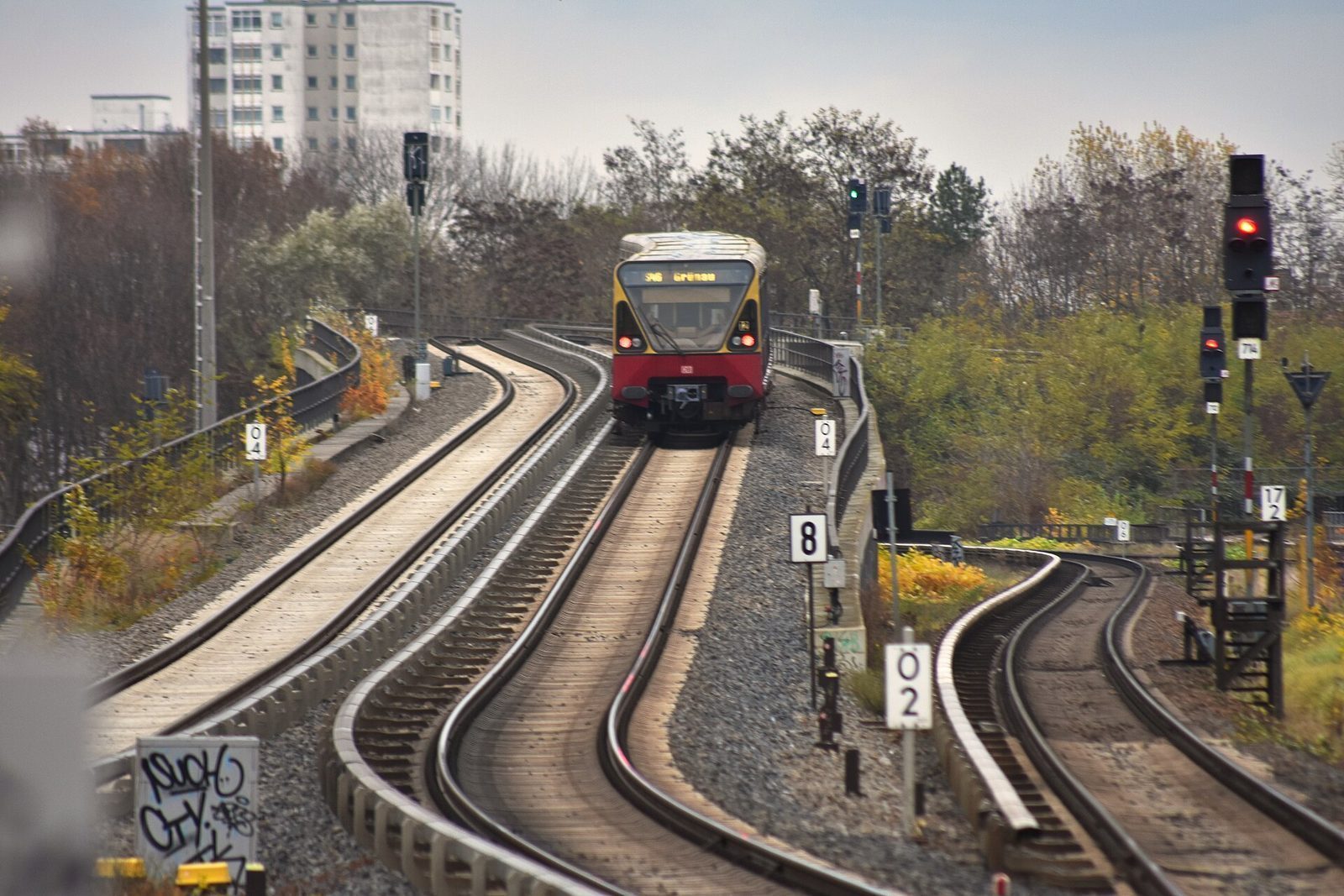 Rod-gult S-Bahn-tog pa vei inn i en kurve mellom hostgule traer
