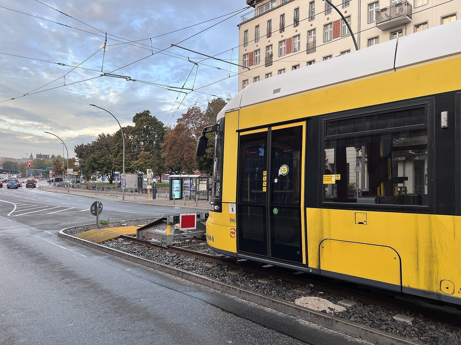 Gul BVG-trikk ved holdeplassen pa Warschauer Strasse i skumringen, under kjoreledningene