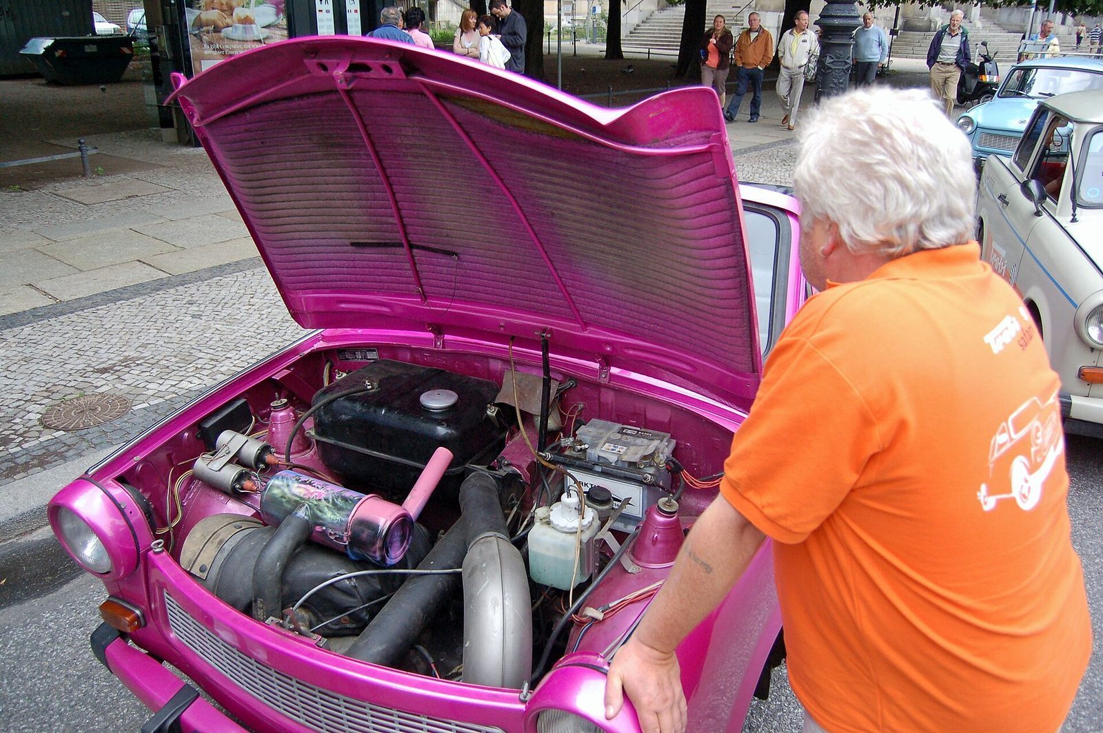 En knallrosa Trabant med panseret oppe som viser den lille tosylindrede motoren, med en Trabi-Safari-vert ved siden