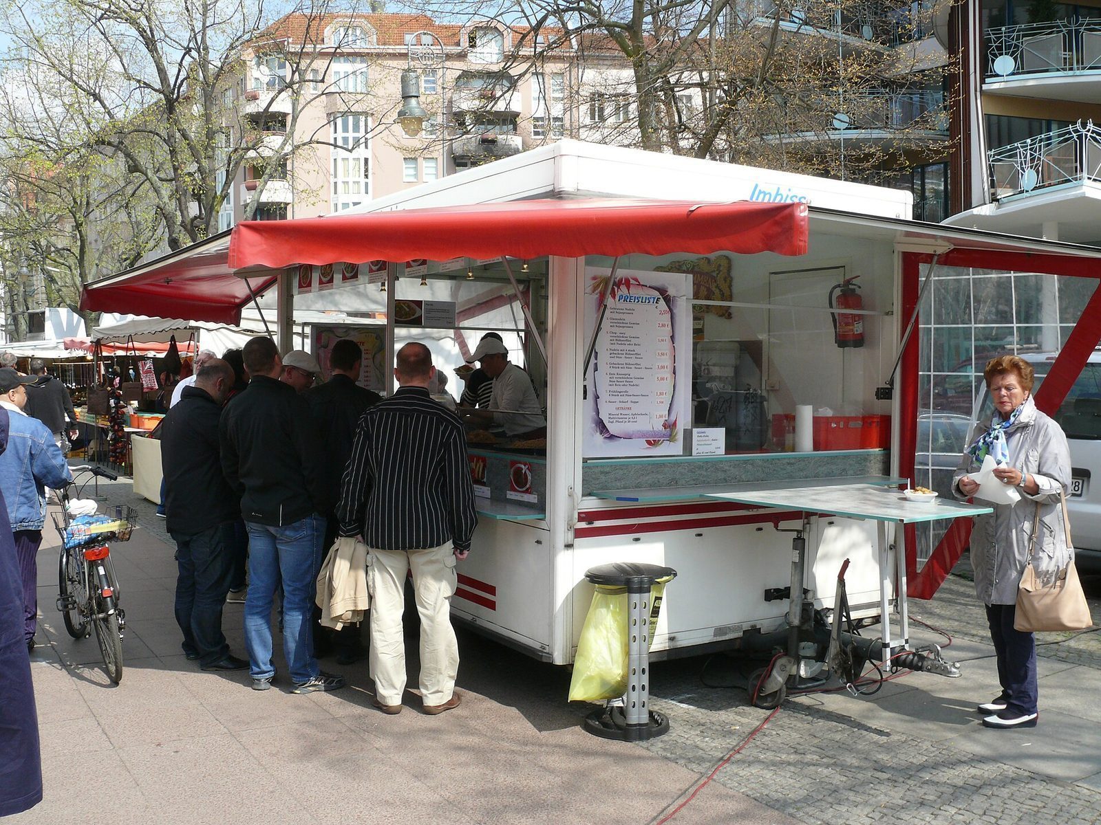 Matbod på torgmarkedet på Winterfeldtplatz, med skiltede retter og gjester ved disken