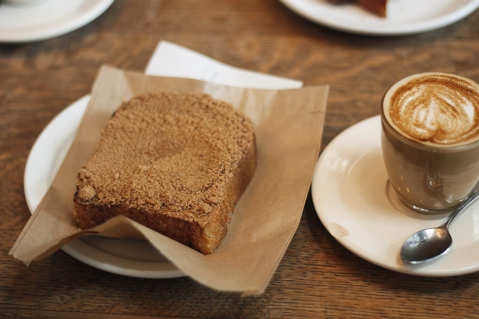 Skive kanelbrød på smørpapir ved siden av en cappuccino med latte art